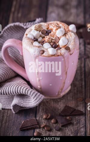 A pink mug with luxurious hot chocolate with whipped cream. On top of the cream are pieces of marshmallows and chocolate chips, and there are pieces o Stock Photo