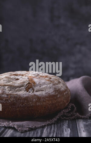 Homemade organic sourdough bread, side view. The cracked rustic bread is laid on a linen cloth, which is on a rustic dark wooden table with gray backg Stock Photo