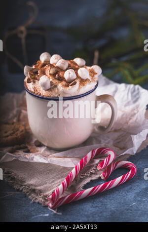 Luxurious hot chocolate with whipped cream and pieces of marshmallows and chocolate chips, in a white mug on a blue background. In front of the chocol Stock Photo