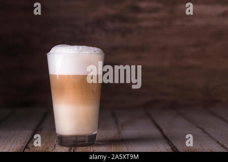 Coffee cafe latte macchiato in a high glass on a wooden background. There is copy space next to the glass, and the photo is horizontal. Stock Photo