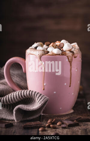 A pink mug with luxurious hot chocolate with whipped cream. On top of the cream are pieces of marshmallows and chocolate chips. Side view. Vertical sh Stock Photo