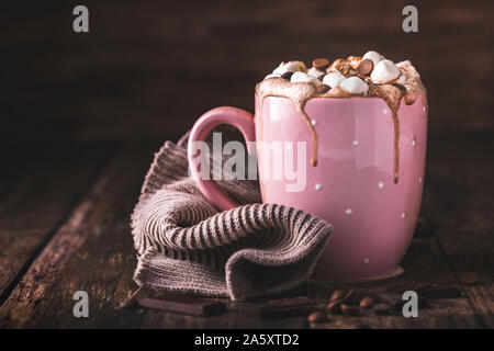 A pink mug with luxurious hot chocolate with whipped cream. On top of the cream are pieces of marshmallows and chocolate chips. Side view. Horizontal Stock Photo