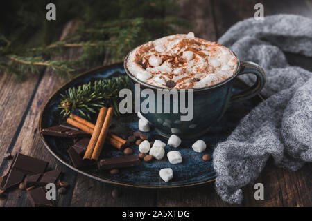 A blue handmade ceramic mug with luxurious hot chocolate  with whipped cream on top There are small pieces of marshmallows and chocolate chips on the