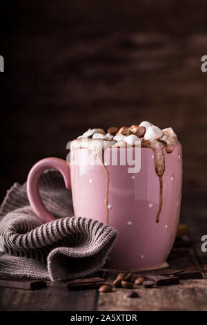A pink mug with luxurious hot chocolate with whipped cream. On top of the cream are pieces of marshmallows and chocolate chips. Side view. Stock Photo