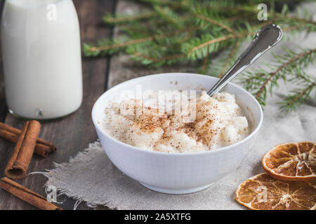 Traditional rice pudding also known as tomtegröt or swedish risgrynsgröt. The rice pudding is in a white porcelain bowl on a dark  wooden table, with Stock Photo