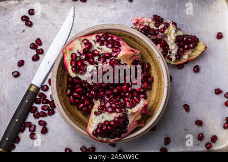Pomegranate slices and seeds in a ceramic bowl. The fruits are on a metal background, and there are also some pomegranate seeds next to the bowl. From Stock Photo