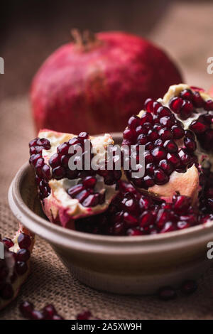 Pomegranate slices and seeds in a ceramic bowl. The fruits are on a rustic jute textile, and there are also some pomegranate seeds next to the bowl. V Stock Photo