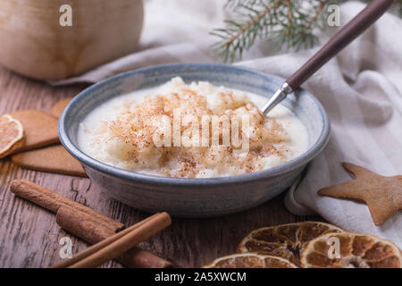 Traditional rice pudding also known as tomtegröt or swedish risgrynsgröt. The rice pudding is in a blue ceramic bowl on a wooden table, with gingerbre Stock Photo