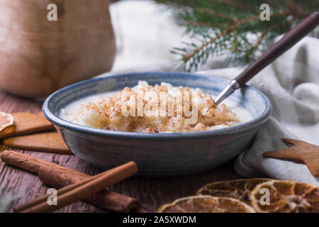 Traditional rice pudding also known as tomtegröt or swedish risgrynsgröt. The rice pudding is in a blue ceramic bowl on a wooden table, with gingerbre Stock Photo