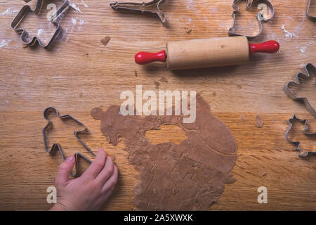 Gingerbread baking on a wooden table, with a kids hand grabbing one of the cookie cutters.  There are cookies cutters in various shapes on the table, Stock Photo