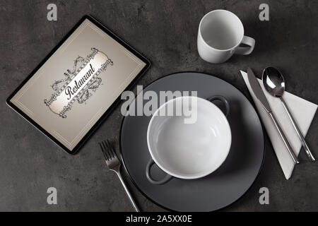 Tablet with stylish restaurant logo and laid table Stock Photo