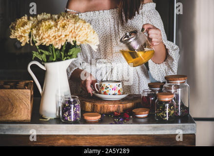 Young woman pouring green tea from pot into cup Stock Photo