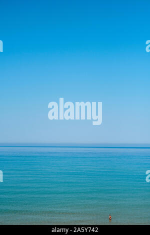 A deep blue sea and sky horizon with a lone isolated figure relaxing in the sea - a lone figure in an endless blue seascape Stock Photo