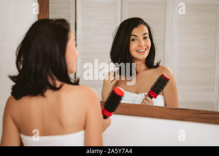 Gorgeous smiling woman brushing healthy hair in front of the mirror. girl combing her hair Stock Photo