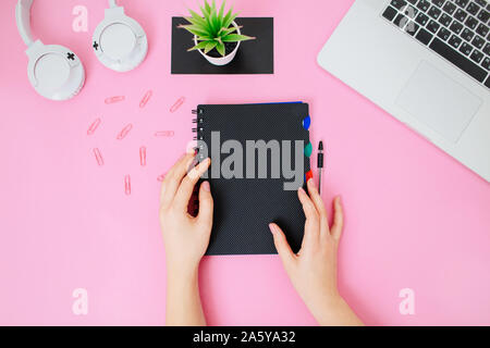 Stylized flatlay with female office desk. Workplace with laptop, computer mouse, notepad in woman's hand, succulent and headphones. Copy space. Stock Photo