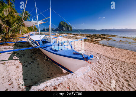 Traditional banca boat at exotic sandy beach with amazing Pinagbuyutan tropical island in background. Exotic nature scenery in El Nido, Palawan Stock Photo
