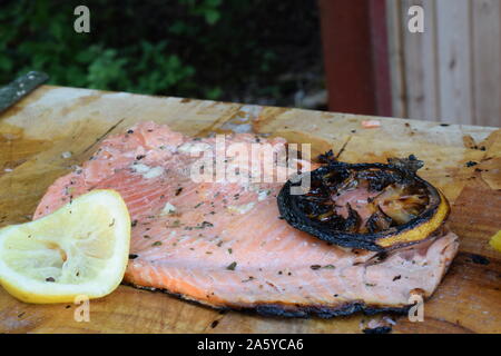 Grilled salmon fillet and lemon slices on wooden cutting board. Stock Photo