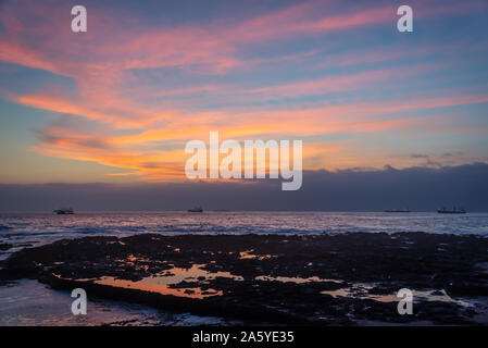 Sunset on the coast of Pacific ocean in Arica, Chile. Boats in the background Stock Photo