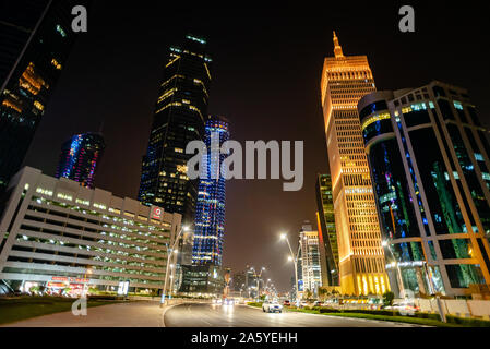 A quiet urban street in the financial district of Doha at night. The Al Asmakh Tower is seen illuminated in yellow lighting Stock Photo