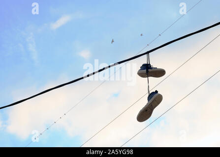 Sports shoes dangling on power cable. Pair of old sneakers hanging on electric wires Stock Photo