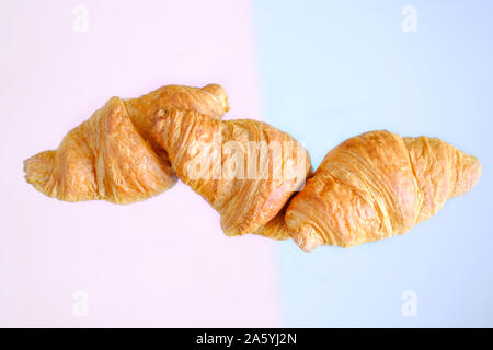 Three freshly baked croissants fly on pink and blue background. Place for text. Creative bakery concept Stock Photo