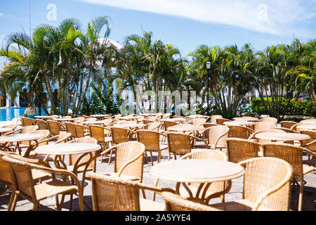 contrast view of open-air cafe with tables and chairs and background of palms Stock Photo