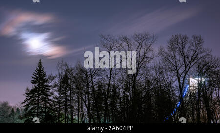 Colorful moon rising above trees and tower in winter Stock Photo