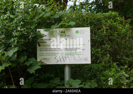 A defaced environmental crime watch area notice in English and Welsh posted by the Welsh government warning offenders of large fines for fly tipping Stock Photo