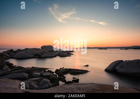 Long exposure image of yacht moored in a bay as the sun sets over the Mediterranean sea and large granite boulders on the coast of Cavallo Island in t Stock Photo