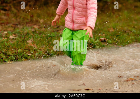 Little Cute Playful Caucasian Blond Toddler Boy Enjoy Have Fun Playing  Jumping In Dirty Puddle Wearing Blue Waterproof Pants And Rubber Rainboot  At Home Yard Street Outdoor Happy Childhood Concept Stock Photo