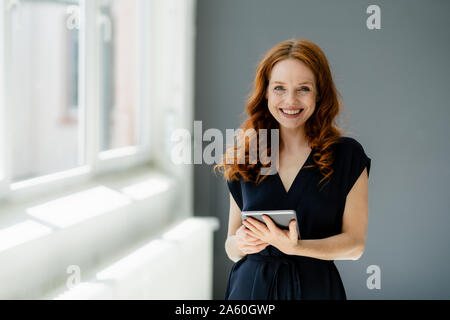 Portrait of content redheaded businesswoman with digital tablet in a loft Stock Photo