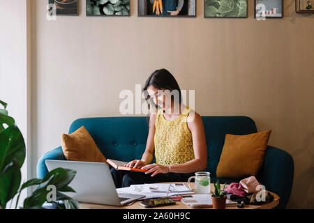 Smiling fashion designer sitting on couch working on a new collection Stock Photo