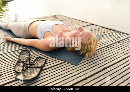 Young woman lying on a jetty at a lake Stock Photo