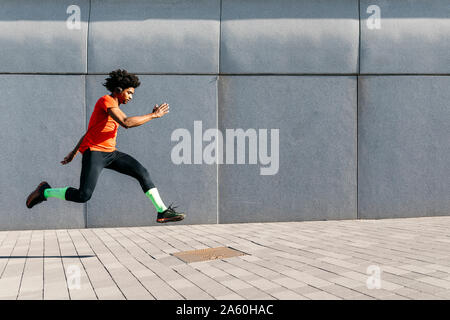 Young man jumping in front of a gray wall in the city, listening to music Stock Photo