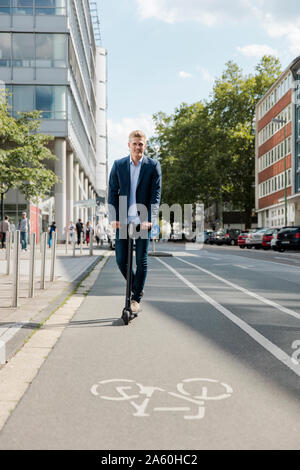 Young businessman riding e-scooter on bicycle lane in the city Stock Photo