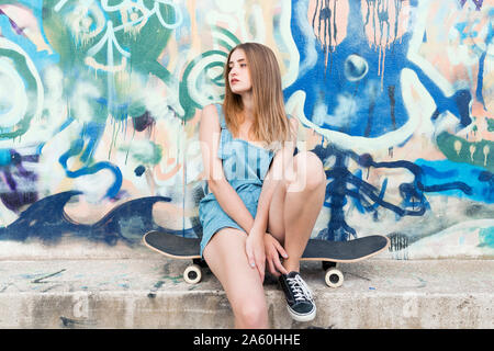 Young woman sitting on skateboard in front of graffiti Stock Photo