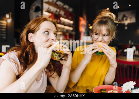 Two female friends eating burger in a restaurant Stock Photo