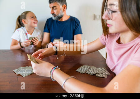 Father with two daughters playing cards on wooden table at home Stock Photo