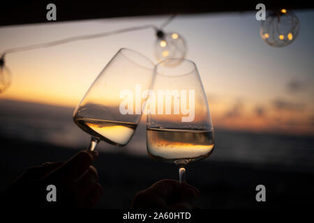 Woman holding two glasses of white wine in van at sunset Stock Photo