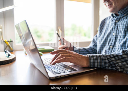Senior man using laptop and smartphone at home Stock Photo
