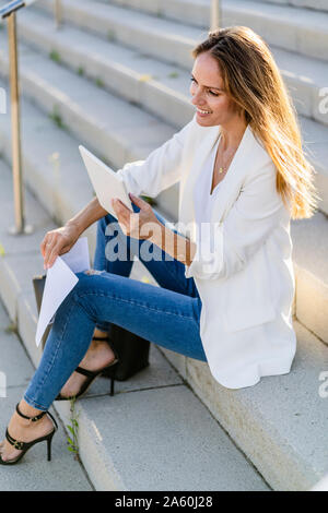 Businesswoman sitting on stairs with paper and tablet Stock Photo