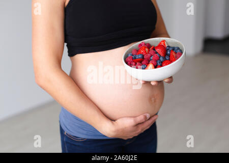 Young pregnant woman is eating different kinds of fresh fruits Stock Photo