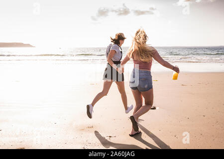 Two girlfriends having fun, running and jumping on the beach Stock Photo