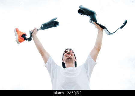 Happy young man with leg prosthesis cheering under cloudy sky Stock Photo