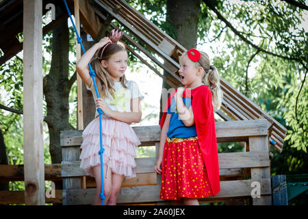 Girls dressed up as princess and superwoman playing in a tree house Stock Photo