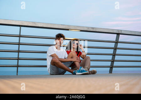 Young couple sitting on bridge by the sea Stock Photo