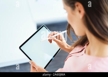 Over the shoulder view of woman drawing on tablet using pencil Stock Photo