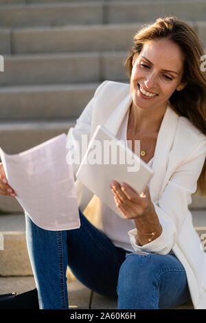 Businesswoman sitting on stairs with paper and tablet Stock Photo