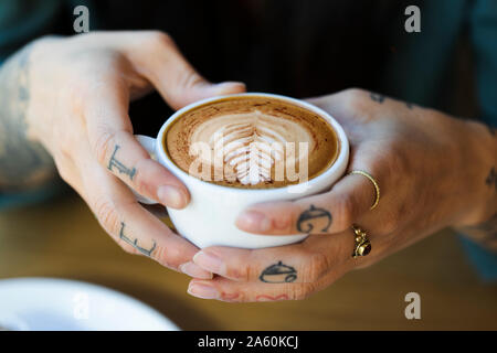 Tattooed hands holding cup of cappuchino Stock Photo