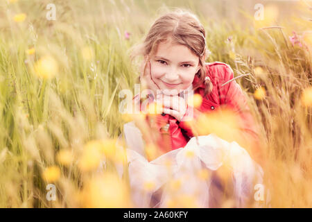 Portrait of smiling girl wearing red leather jacket crouching in flower meadow Stock Photo